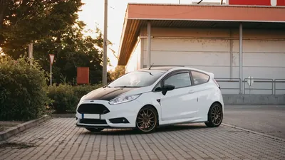 A white compact hatchback parked in front of a building at sunset
