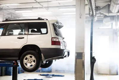 A car raised on a two-post lift inside a workshop, seen from the side