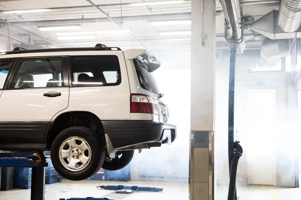 A car raised on a two-post lift inside a workshop, seen from the side