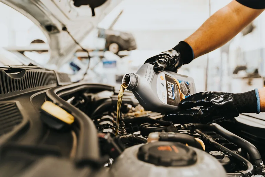 A gloved hand pouring fresh engine oil into a car's engine bay