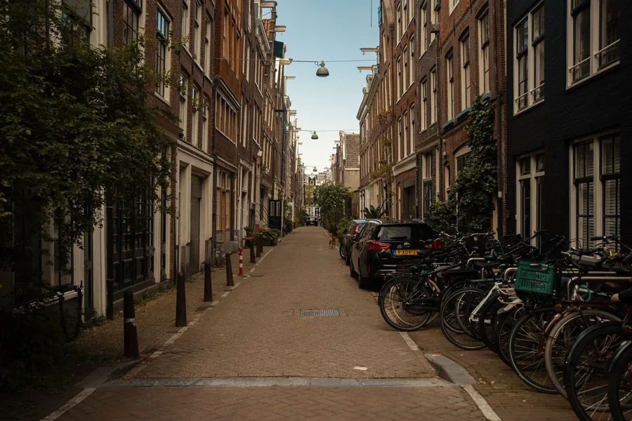 A narrow Dutch street with parked bicycles and cars beside brick buildings