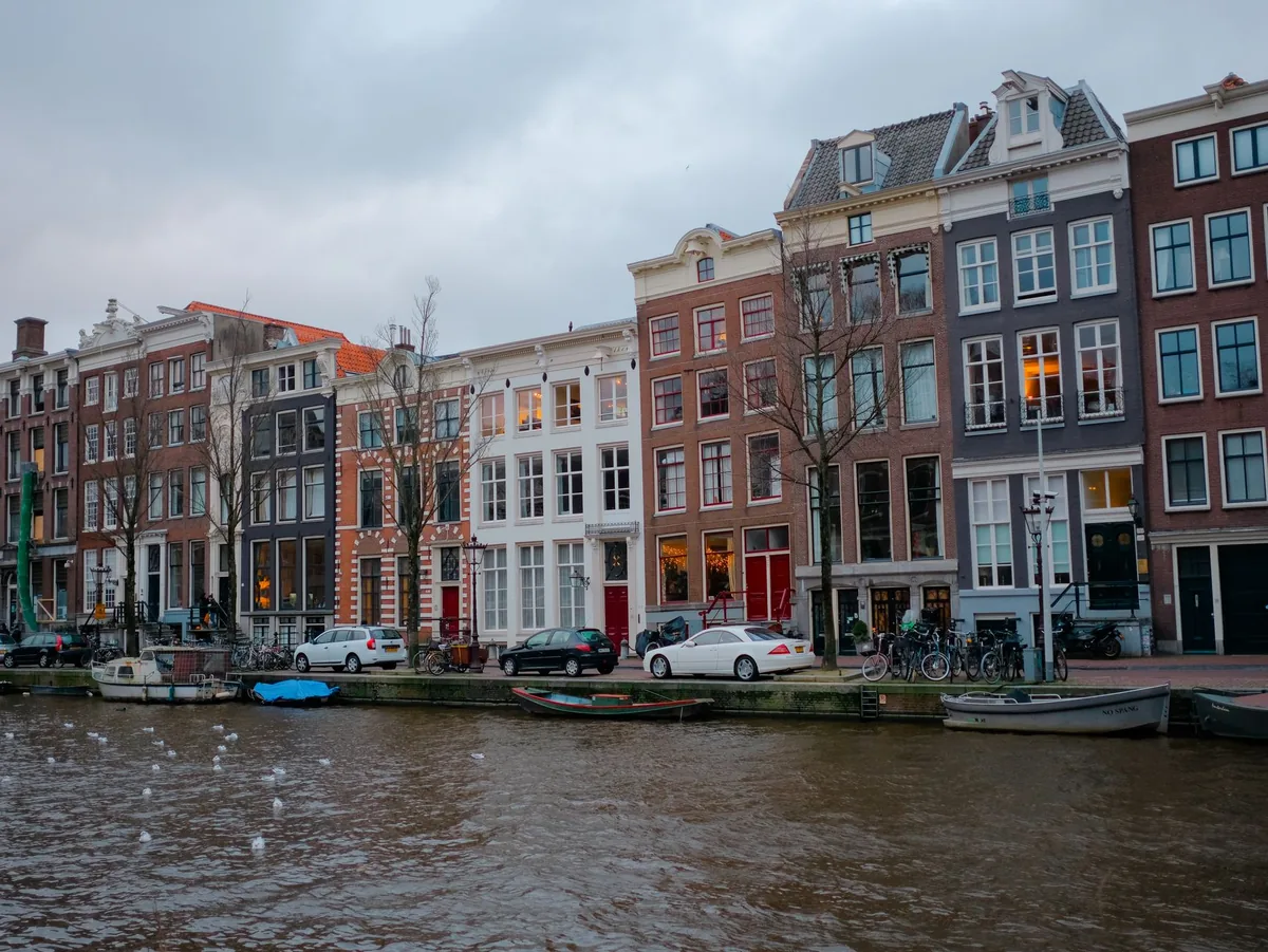Canal houses in Amsterdam with cars and bicycles parked along the quay