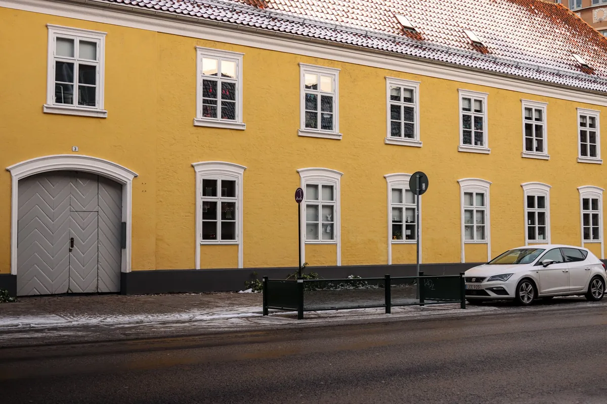 A white hatchback parked on a snow-dusted street outside a yellow brick building in Malmö, Sweden