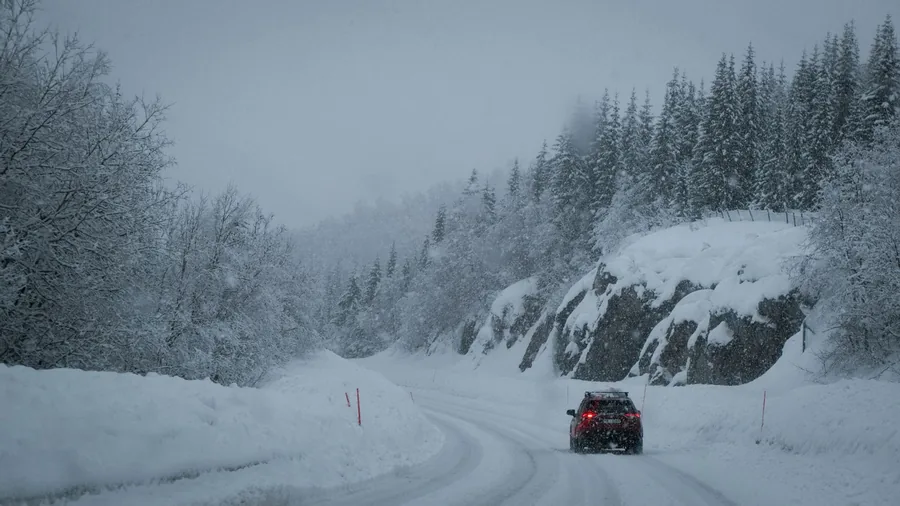 A car driving along a snow-covered road between snowbanks in winter