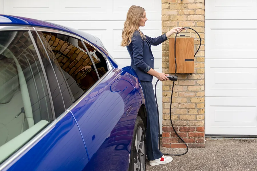 A driver connecting a charging cable to an electric car at a home wallbox