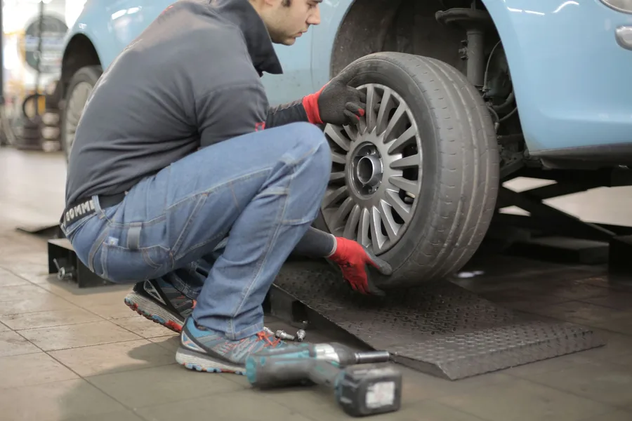 A mechanic fitting a wheel to a car raised on a lift in a workshop