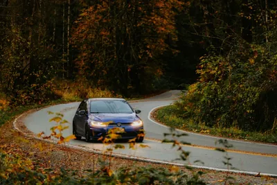 A car driving along a winding two-lane road lined with autumn trees