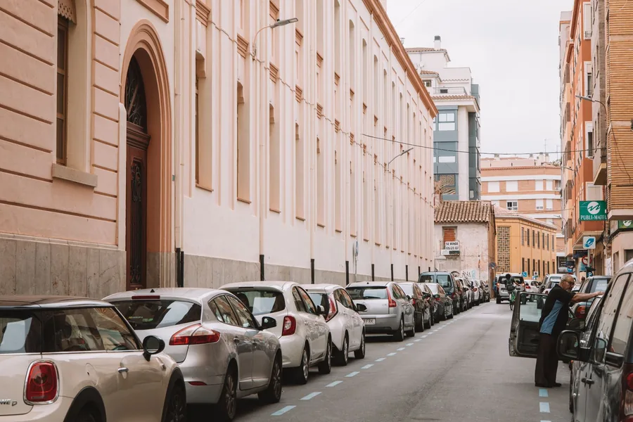 A narrow Spanish street lined with parked cars on both sides