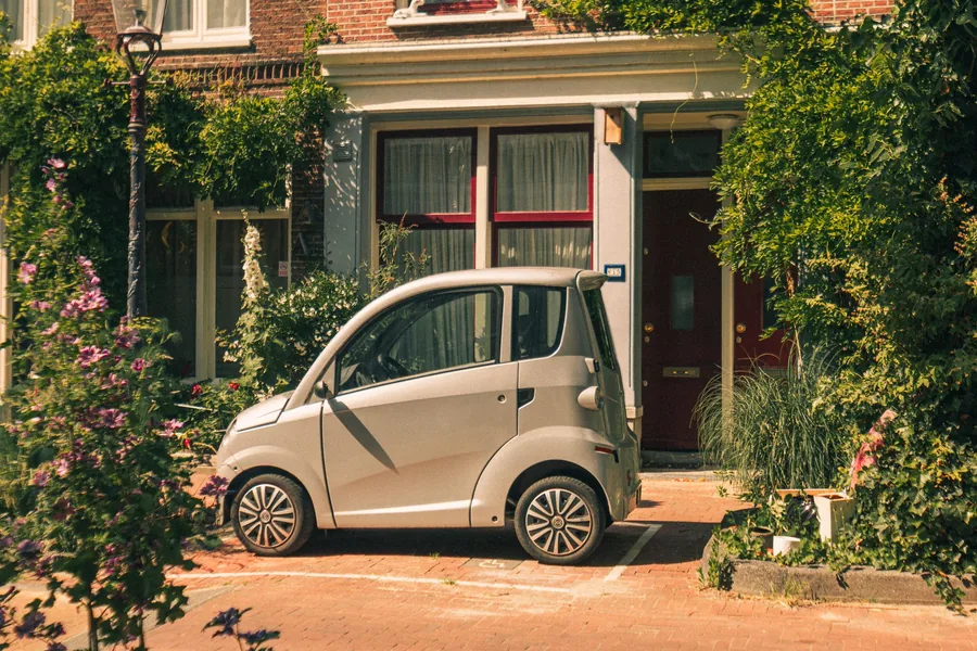A small city car parked in a brick-paved bay in front of a Dutch townhouse