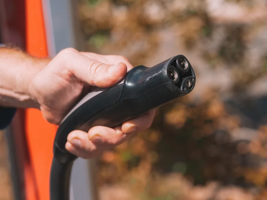A hand holding a Type 2 electric vehicle charging connector