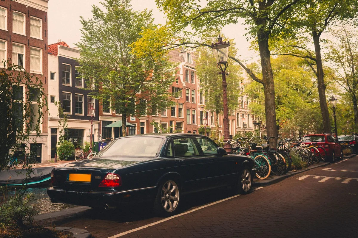 A car parked on a brick-paved street beside an Amsterdam canal lined with bicycles