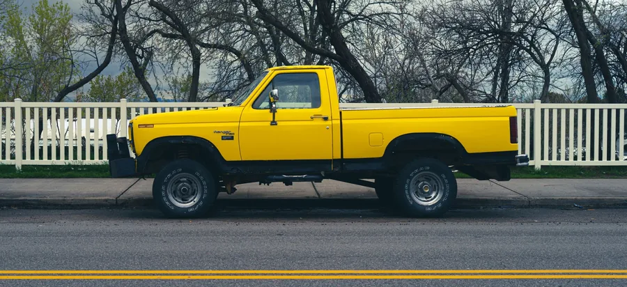 A pickup truck parked beside a road with trees behind it