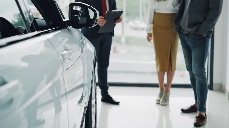 A salesperson with a clipboard beside a car in a showroom