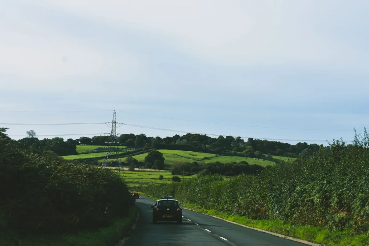 A car on a narrow rural road between hedgerows with green fields and rolling hills