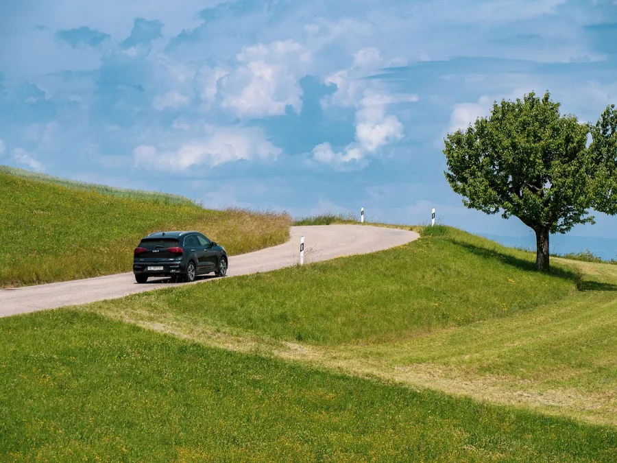 A car driving away along a winding rural road between green fields
