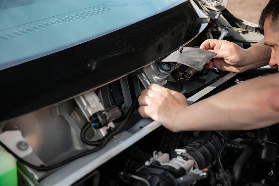 Close-up of hands working in a car engine bay with the bonnet open