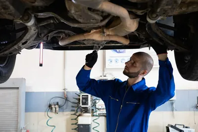A mechanic working under a car raised on a lift with an inspection light