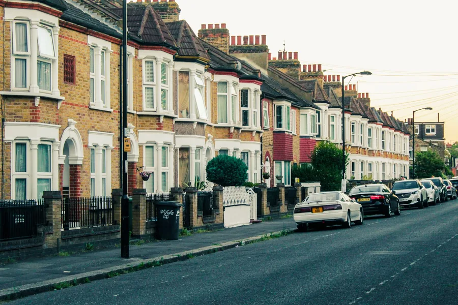A small white hatchback parked on a residential street of red-brick terraced houses in the UK