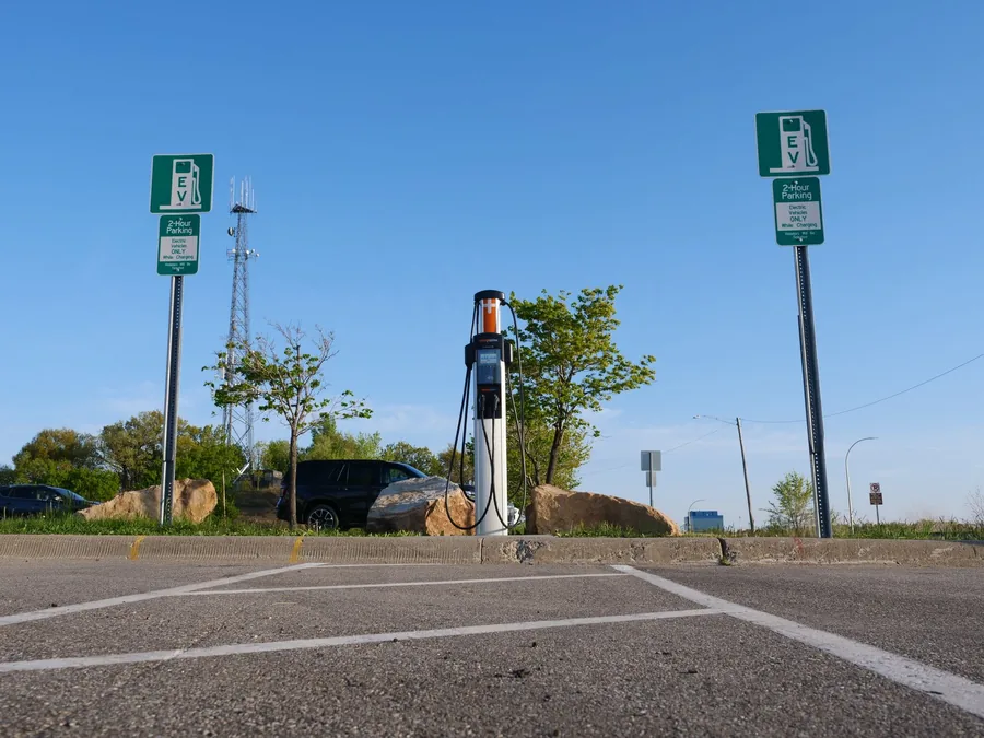A public fast charger pedestal beside parking bays marked for electric vehicles only