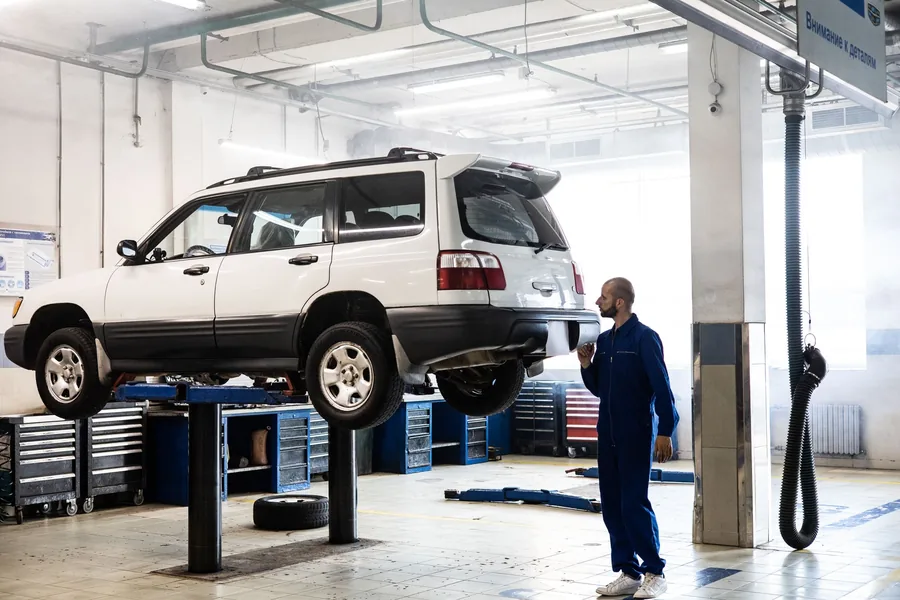 A car raised on a two-post lift in a workshop while a mechanic inspects it