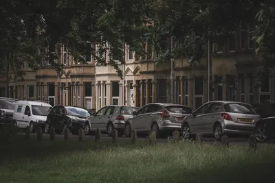 A row of parked cars lining a tree-lined residential street of brick terraces