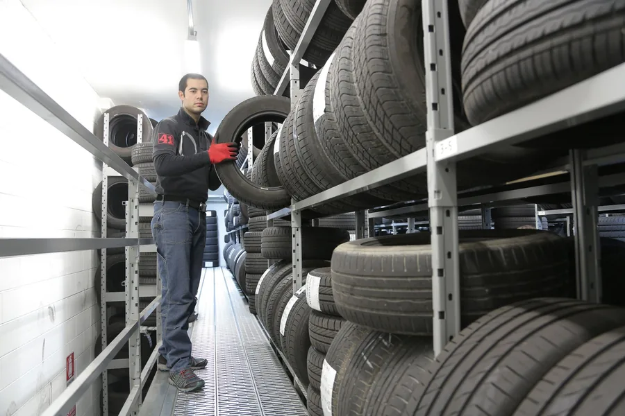 Rows of stacked tyres in a tyre warehouse with a worker walking between them