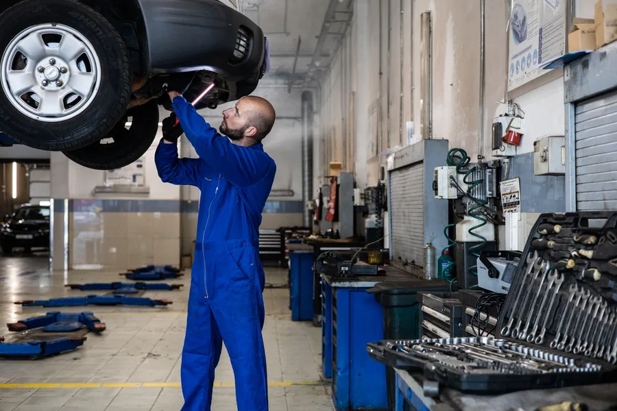 A mechanic inspecting a car raised on a lift in a workshop