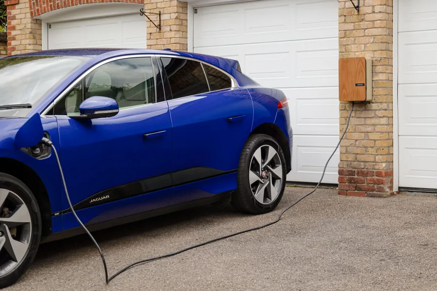 A blue electric car plugged into a home wall-mounted charging unit