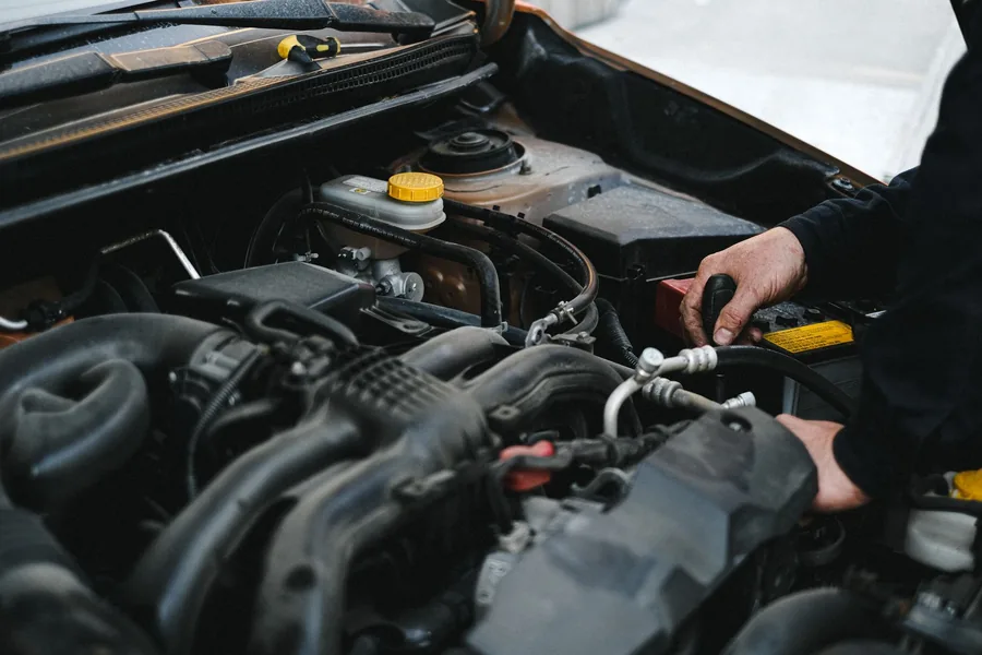 Hands working on a car engine bay with the bonnet open
